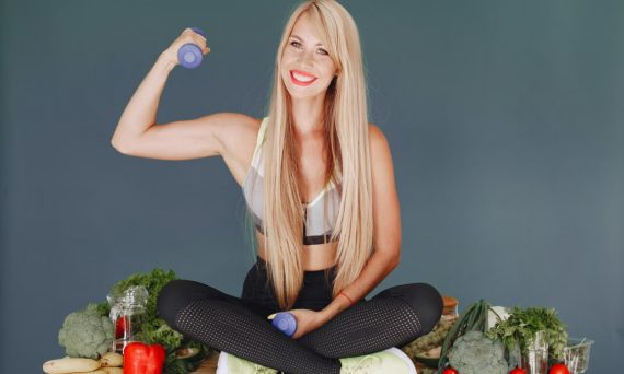 Woman lifting a small dumbbell while surrounded by fresh vegetables, embodying health and fitness.
